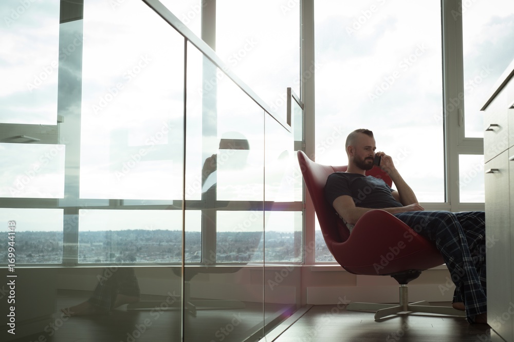 Man talking on mobile phone while sitting on chair in the living Man talking on mobile phone while sitting on chair in the living