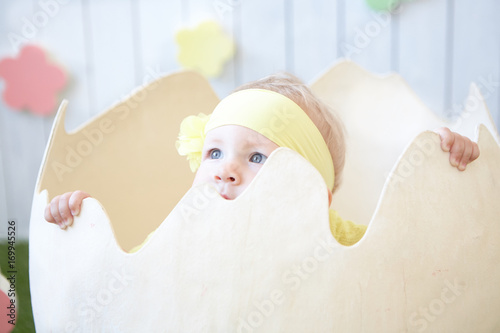little girl in yellow dress with decoration hiding into the eggshell