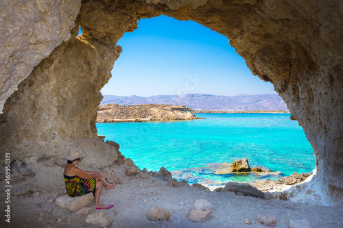 Amazing summer view of woman in a cave at Koufonisi island with magical turquoise waters, lagoons, tropical beaches of pure white sand and ancient ruins on Crete, Greece