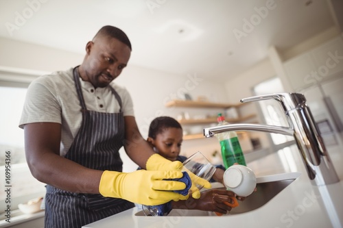 Father and son cleaning utensils in kitchen