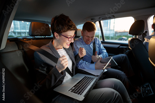 Businesspeople looking at laptop in car on trip. © luckybusiness