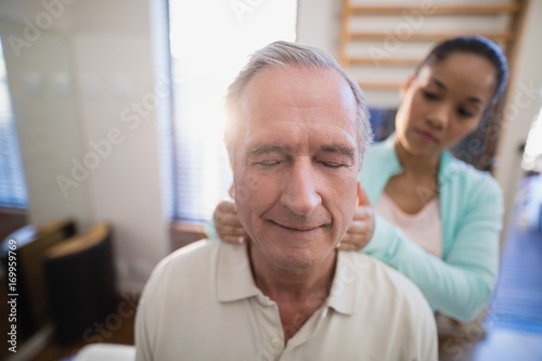 Senior male patient with eyes closed receiving neck massage from