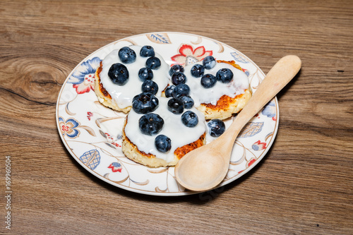 bowl with flowers full of fresh curd pancakes with blueberries. On wood table