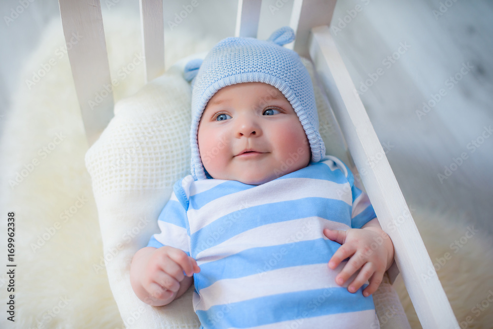smiling newborn baby boy with big blue eyes in a Blue hat lying in