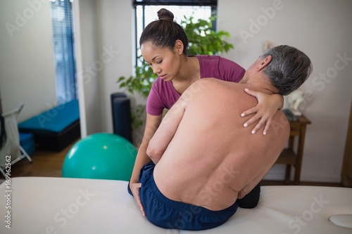 Young female therapist examining buttocks of shirtless senior