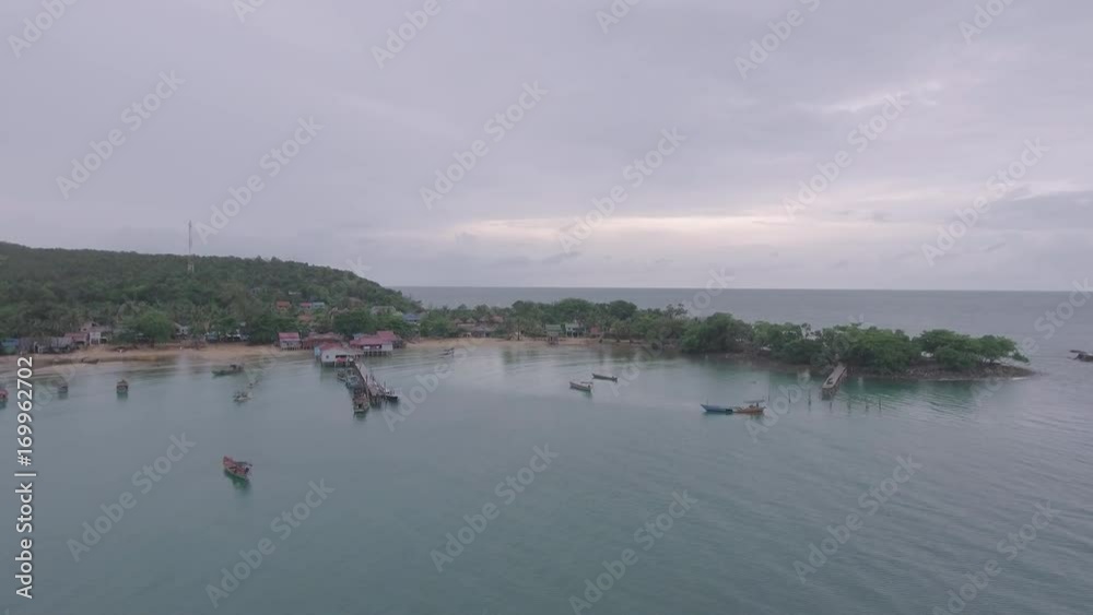 Drone view : Fishing village and fishing boats docked at wooden pier under dark cloudy skies.