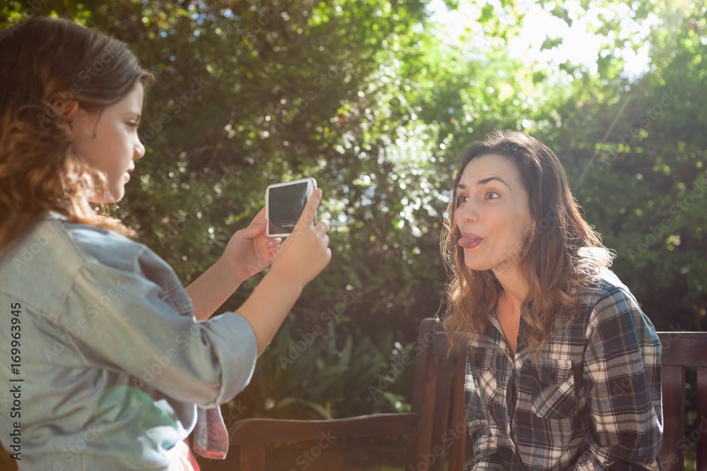 Fototapeta premium Side view of girl photographing mother sticking out tongue