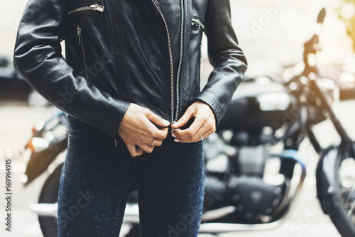 Girl unfastens black leather jacket on background motorcycle in sun flare city, hipster biker female hands closeup, motorbike street lifestyle, traveler planing bike route in summer holiday concept