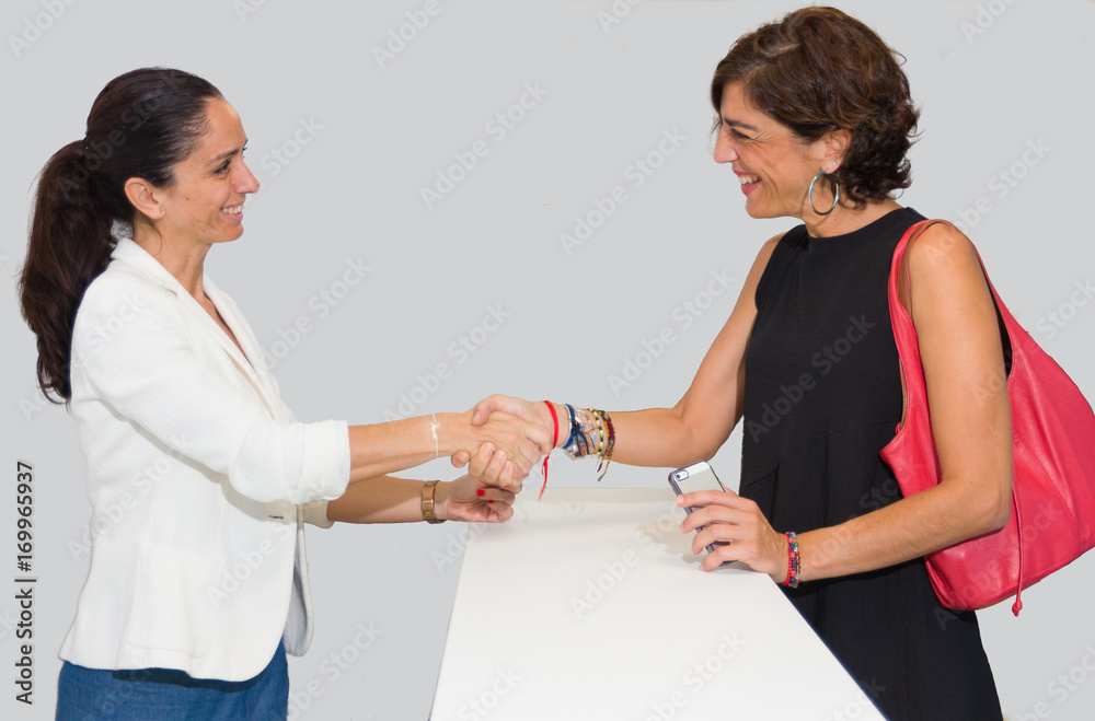 Dos mujeres, empresaria y cliente, dándose la mano sonrientes sobre un mostrador. Dos mujeres, empresaria y cliente, dándose la mano sonrientes sobre un mostrador.
