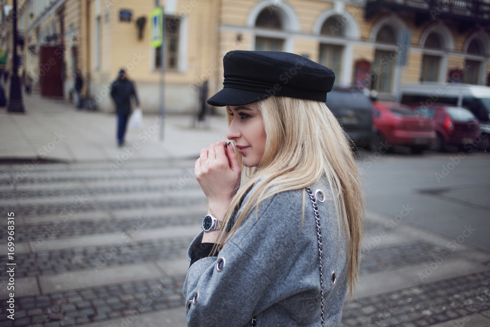 Fototapeta premium My hands were cold. Attractive blonde walking around the city, girl in a stylish hat and a gray coat.