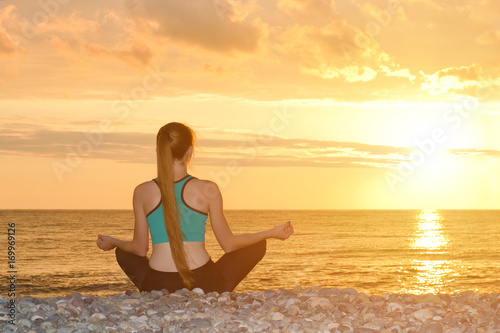 Woman meditating on the beach in lotus position. View from the back  sunset