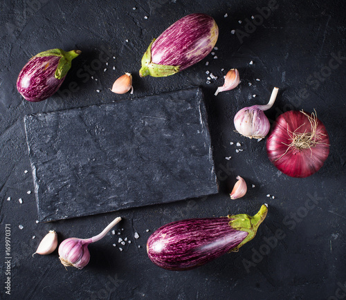 Some eggplants, garlic and red onion on a black board and background. Copy past. Top view.