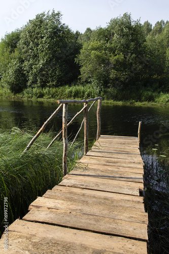 wooden bridge from boards with handrail Summer day on forest river in north of Russia