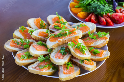 A plate of sandwiches with butter, cheese and red fish on a wooden table on the background of vegetables