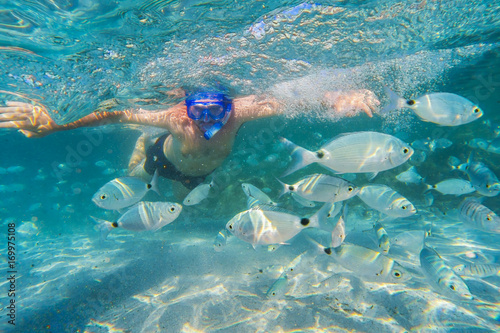Young man snorkeling in underwater coral reef on tropical island.