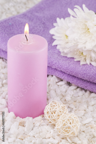 Spa. Still life. Candle of pink color  a towel and white flowers on a background of white pebbles.