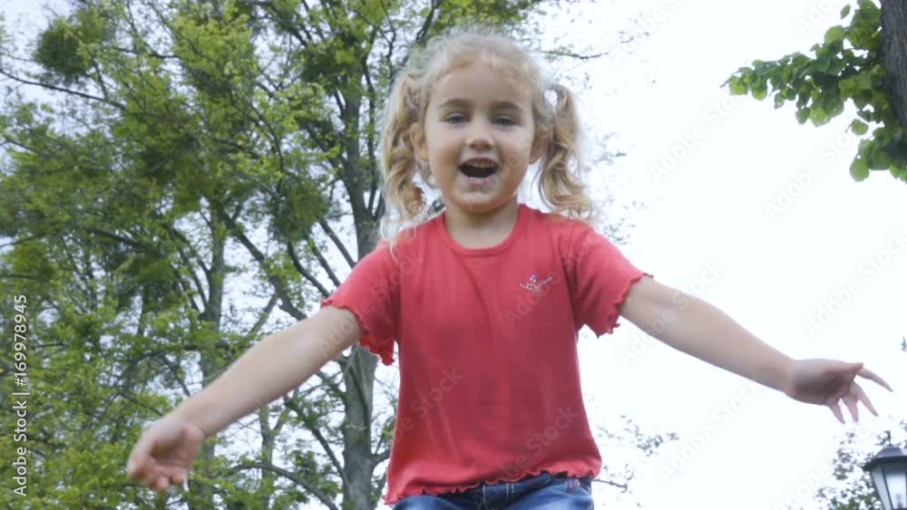 Little child is jumping from a large high stone in the park. Cheerful happy girl in a red T-shirt and jeans jumping on a rock. Slow motion. Little child is jumping from a large high stone in the park. Cheerful happy girl in a red T-shirt and jeans jumping on a rock. Slow motion.
