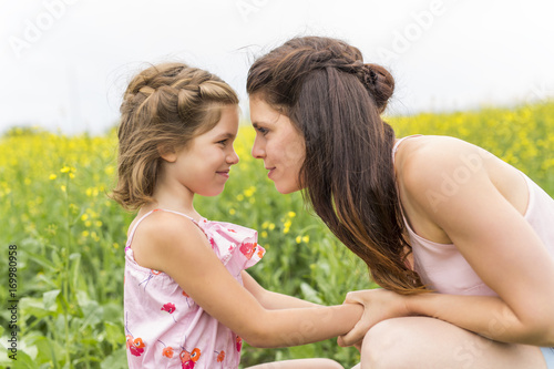 Happy family mother and child daughter embrace on yellow flowers on nature in summer