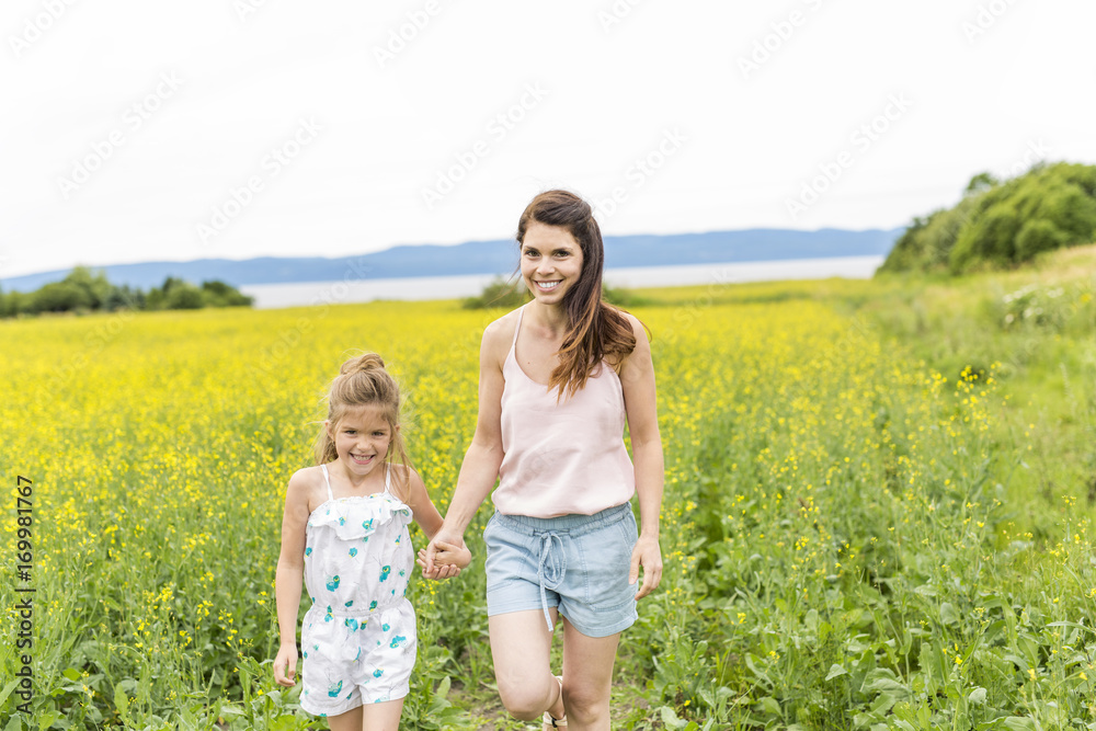 Happy family mother and child daughter embrace on yellow flowers on nature in summer Happy family mother and child daughter embrace on yellow flowers on nature in summer