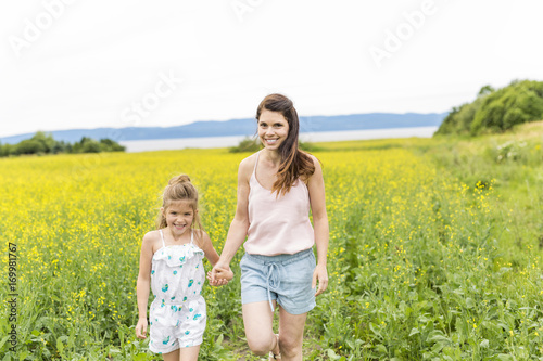 Happy family mother and child daughter embrace on yellow flowers on nature in summer © Louis-Photo