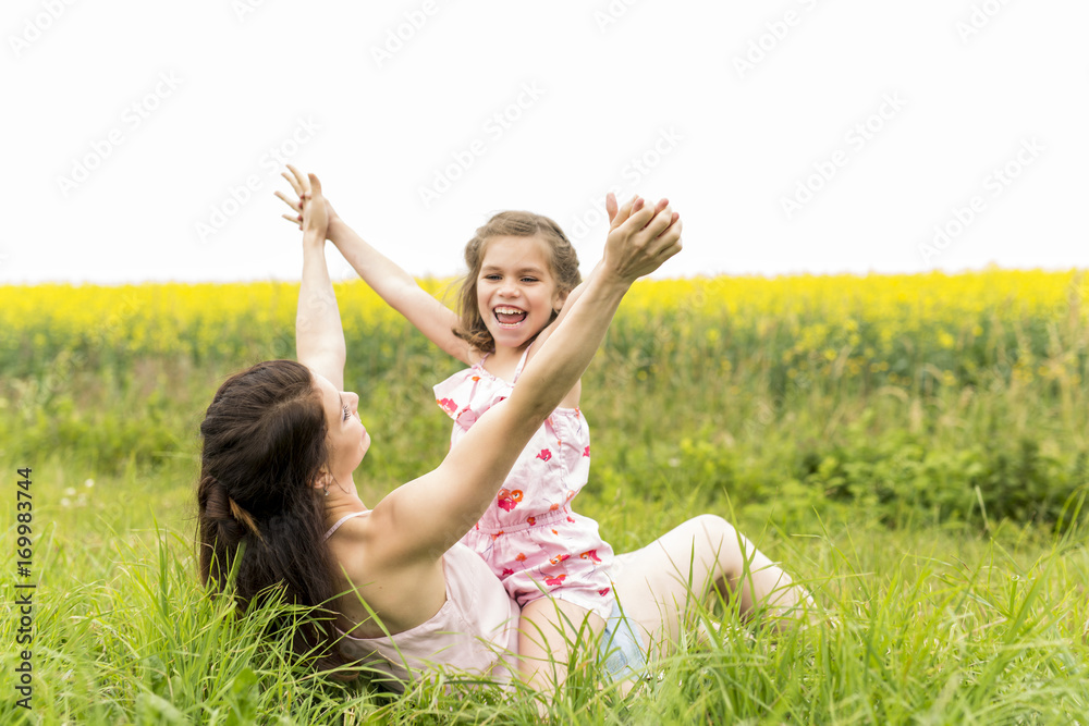 Happy family mother and child daughter embrace on yellow flowers on nature in summer Happy family mother and child daughter embrace on yellow flowers on nature in summer