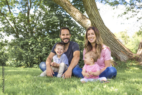 Parents Sitting With Children In Field close to a tree photo