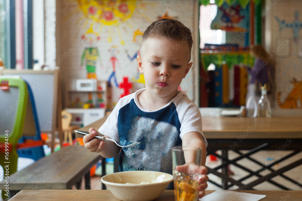 Portrait of Cute little caucasian 3 years old toddler boy child drinking fruit juice in a glass, Smiling boy sitting at restaurant (cafe, hotel) holding glass of tasty orange juice Portrait of Cute little caucasian 3 years old toddler boy child drinking fruit juice in a glass, Smiling boy sitting at restaurant (cafe, hotel) holding glass of tasty orange juice