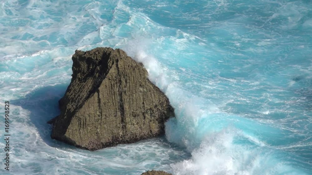 SLOW MOTION CLOSE UP: Turbulent foamy ocean waves breaking over sharp rocky reef. Raging barrel wave hitting the shore splashing over shoal. Powerful surf break crashing into rock spraying water drops