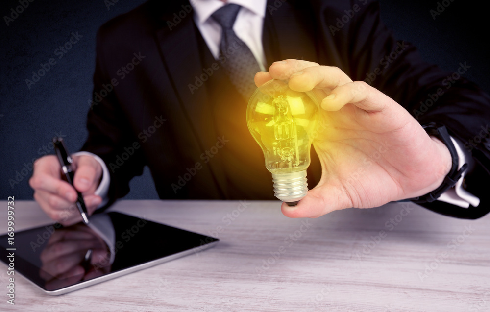 man in suit holding a glowing yellow light bulb - obrazy, fototapety, plakaty 