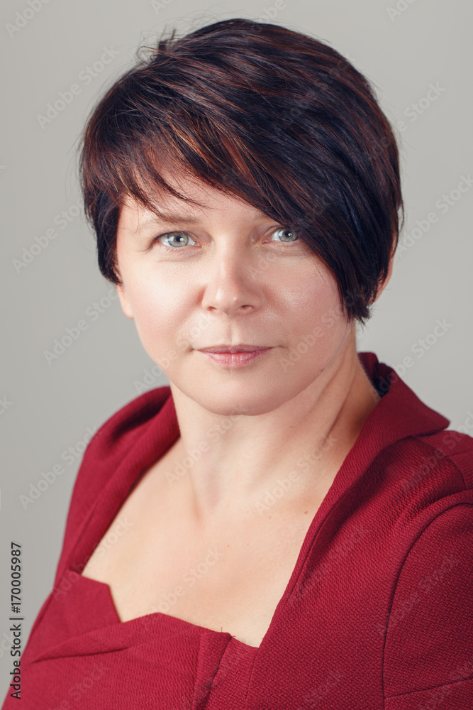 Closeup portrait of beautiful smiling middle aged white caucasian brunette woman with blue eyes in red dress, looking in camera, on light background in studio Closeup portrait of beautiful smiling middle aged white caucasian brunette woman with blue eyes in red dress, looking in camera, on light background in studio