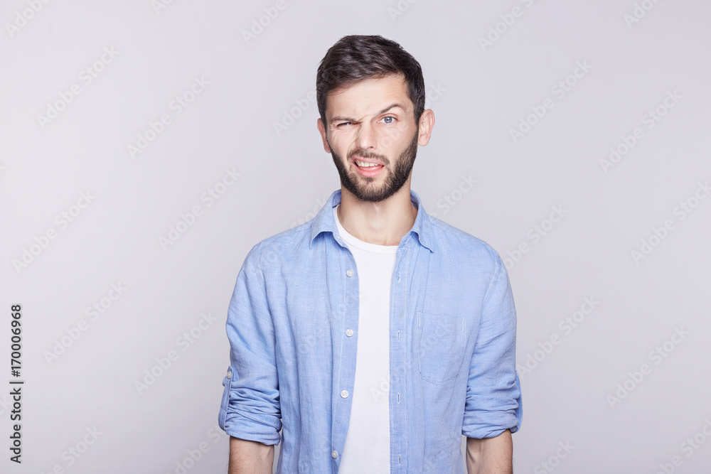 Emotional and stylish young Caucasian blue eyed handsome man employee wearing blue jacket on white t-shirt grimacing, making mouths at camera trying to tease someone, acting like little naughty child. Emotional and stylish young Caucasian blue eyed handsome man employee wearing blue jacket on white t-shirt grimacing, making mouths at camera trying to tease someone, acting like little naughty child.