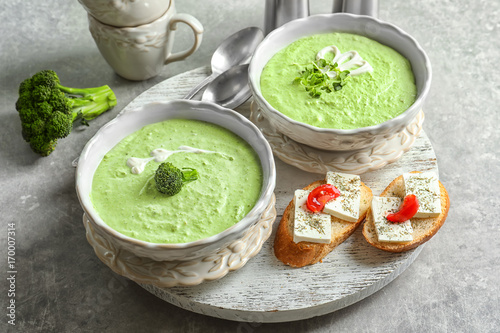 Bowls with delicious broccoli soup on wooden tray