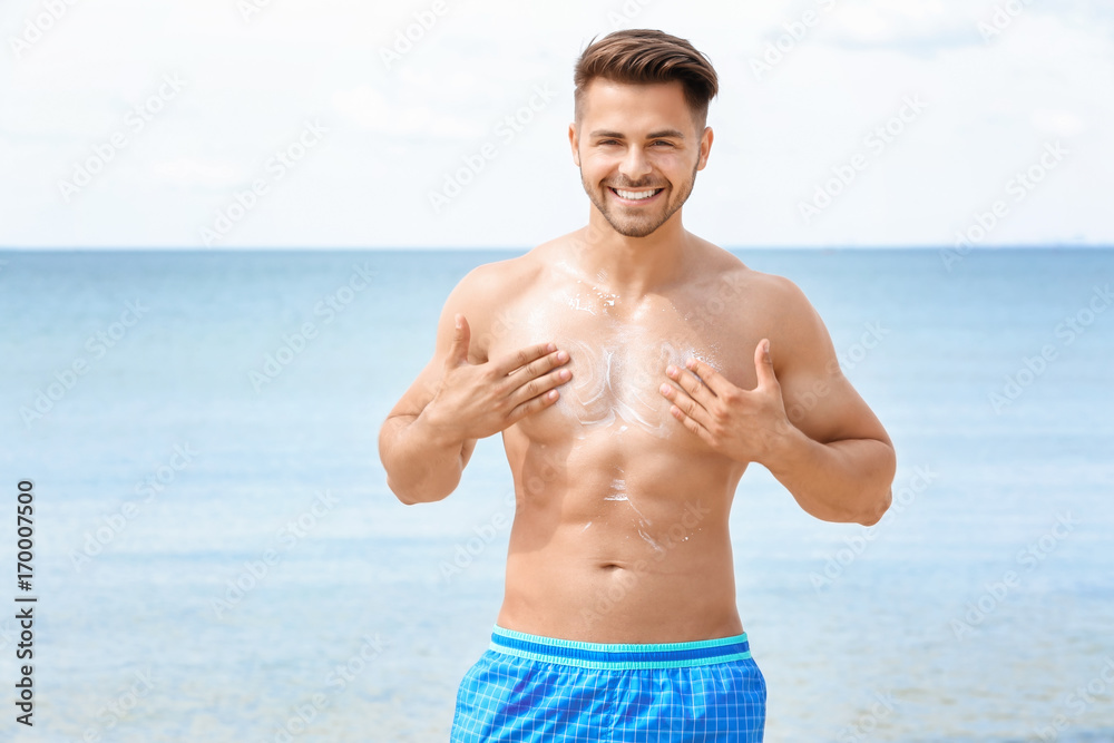 Handsome young man applying sunscreen cream on sea beach Handsome young man applying sunscreen cream on sea beach