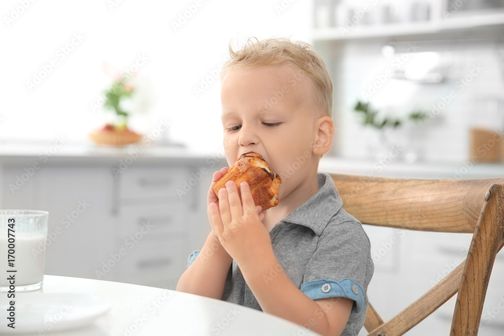 Cute little boy eating big muffin in kitchen Cute little boy eating big muffin in kitchen