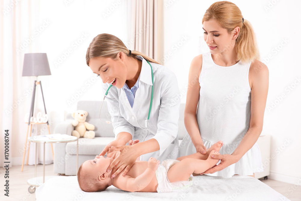Fototapeta premium Young mom standing near couch while doctor examining baby at home