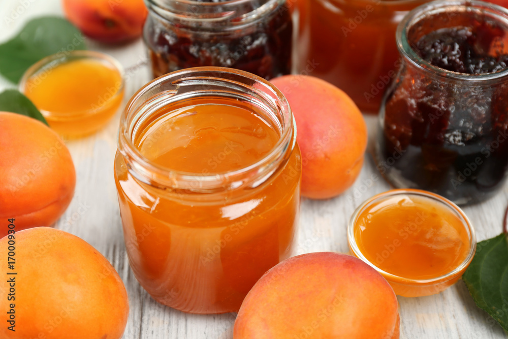 Apricot and berry jams in jars with ripe juicy fruit on wooden table Apricot and berry jams in jars with ripe juicy fruit on wooden table