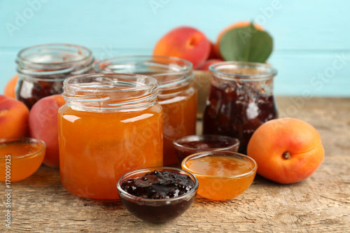 Apricot and berry jams in jars with ripe juicy fruit on table