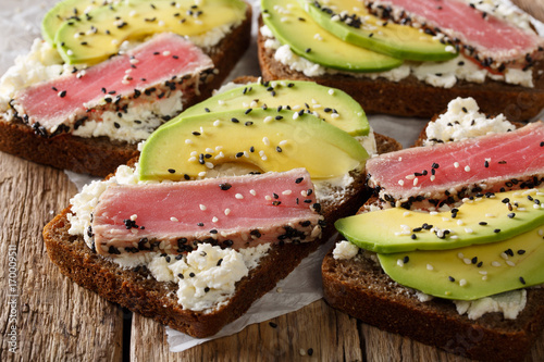 sandwiches with fried tuna in sesame, fresh avocado and cream cheese close-up. horizontal