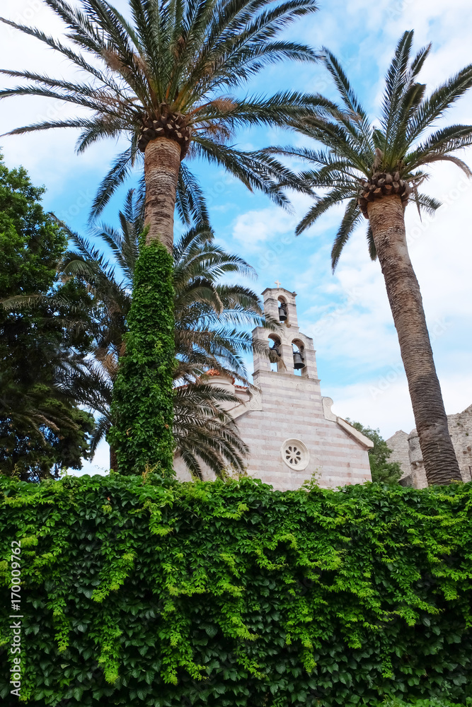 View on old stone chapel through bright green bushes and palm trees View on old stone chapel through bright green bushes and palm trees