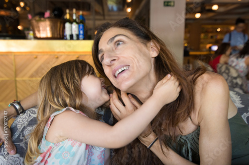 little girl telling a secret in the ear to mother in restaurant