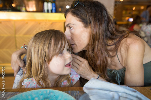 mother telling a secret in the ear to girl in restaurant photo