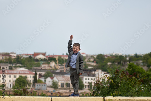 jubilant little boy in a jacket raised one hand up