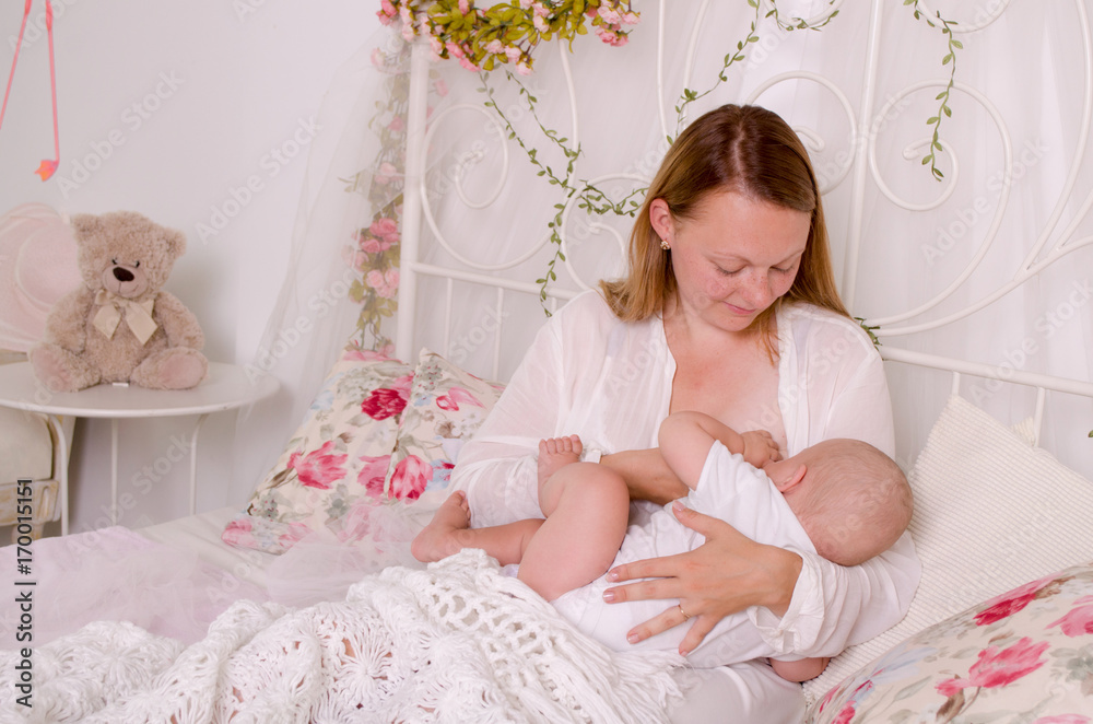 Breastfeeding baby. Young mother holding her newborn child. Mom nursing baby. Woman and new born boy in white bedroom.