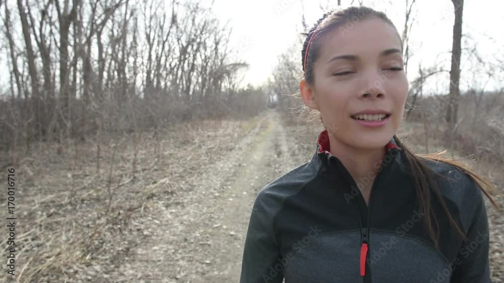Beautiful young woman running on footpath amidst bare trees. Determined female is in sportswear. Confident runner is stretching arms after jogging. She is representing her healthy lifestyle. Beautiful young woman running on footpath amidst bare trees. Determined female is in sportswear. Confident runner is stretching arms after jogging. She is representing her healthy lifestyle.