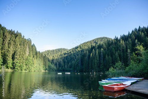 Mountain lake scenery, Lacu Rosu or Red lake with boats near the shore, Eastern Carpathians, Romania, nature landscape background.