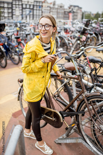 Young woman tourist in yellow raincoat parking a bicycle on the multilevel parking in Amsterdam