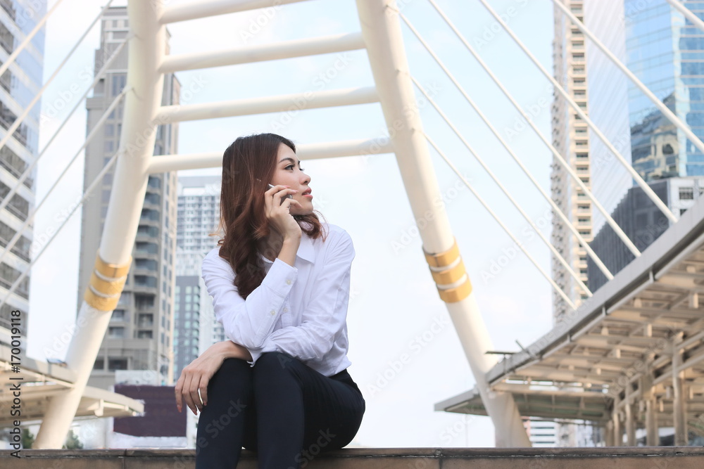 Fornt view of beautiful young Asian woman sitting and talking on phone at urban city background. Fornt view of beautiful young Asian woman sitting and talking on phone at urban city background.