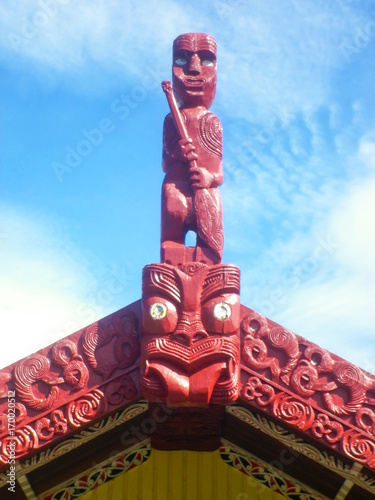 Traditional Maori carved marae on house roof in red color under blue sky