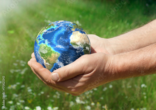 Human holding Earth in hands against green background and sun rays. Ecology concept, earth day. Elements of this image furnished by NASA