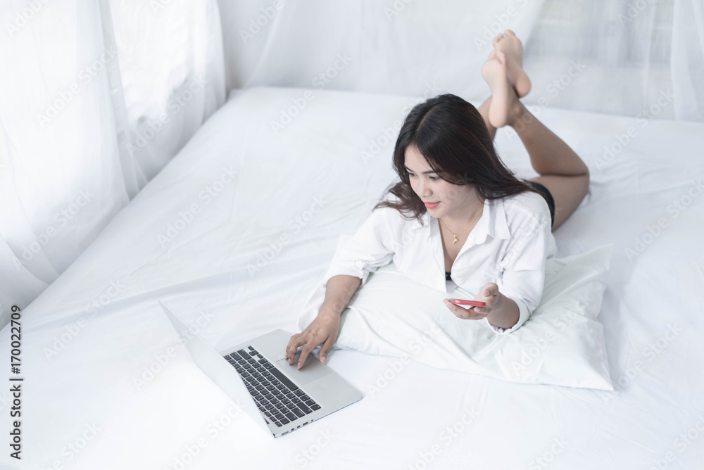 Young woman writing on a computer while in bed